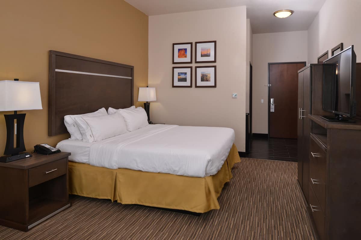 A hotel room with a large bed, a bedside table with a lamp, a TV, and a door leading to another room.