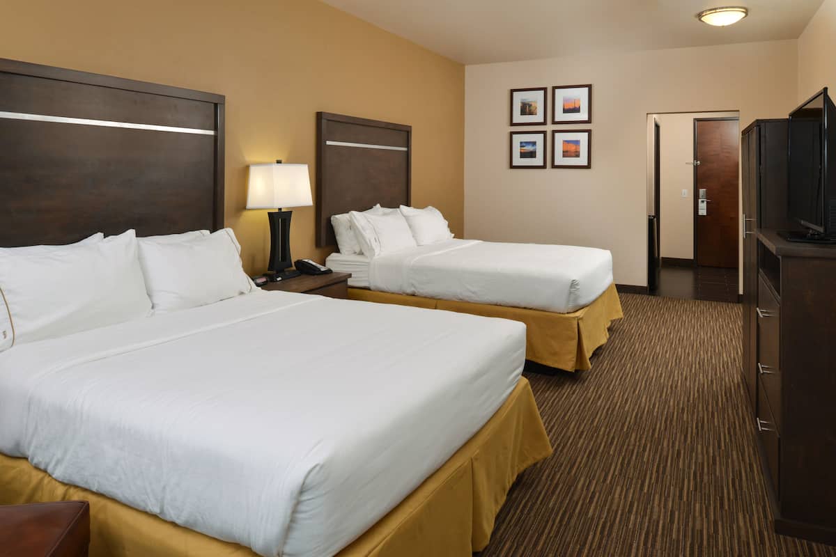 A hotel room with two beds, a desk, a lamp, a television, and framed pictures on the wall.