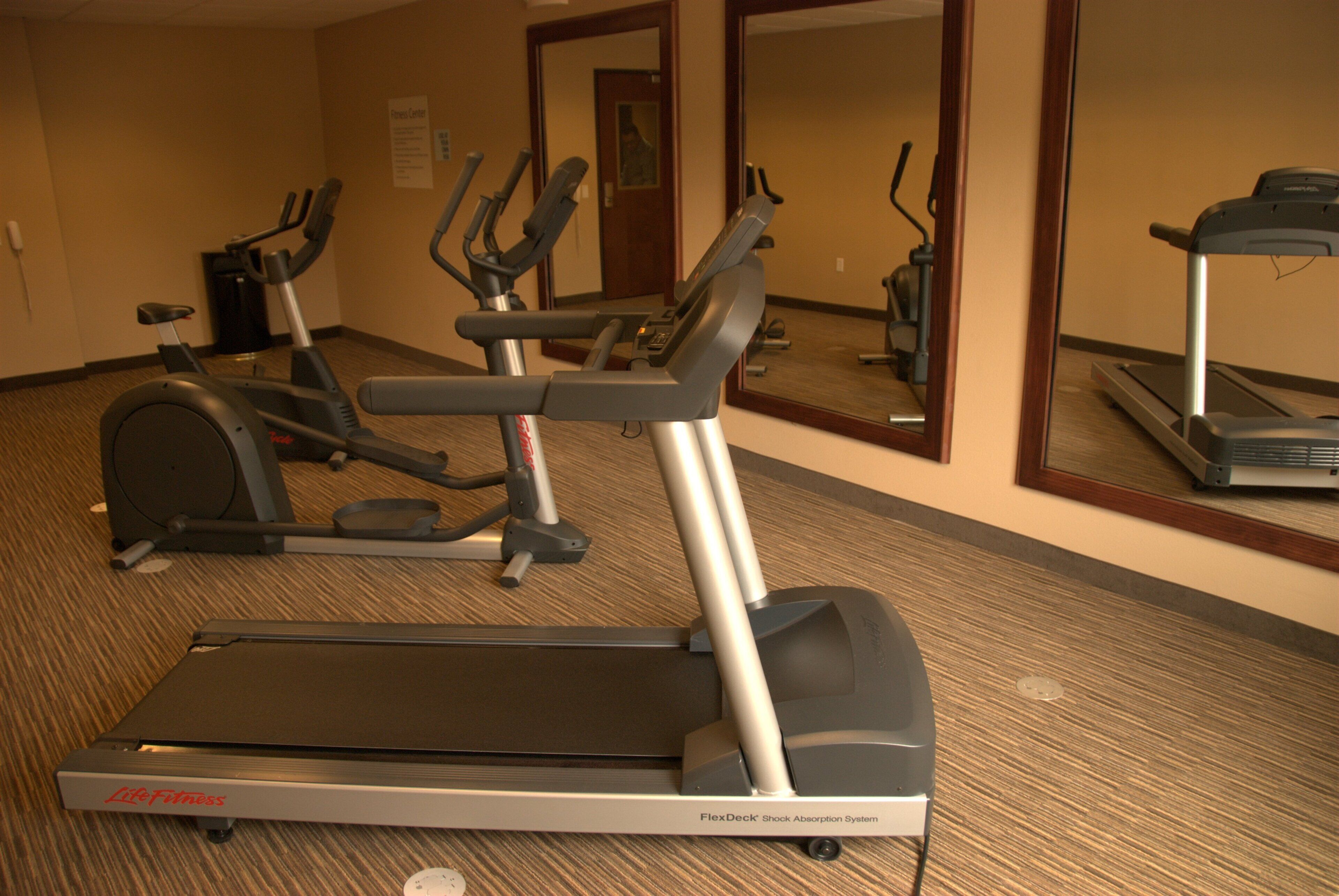 Un gimnasio con cintas de correr, elípticas y un espejo grande.