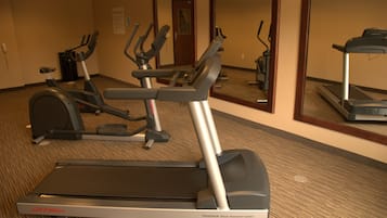 Un gimnasio con cintas de correr, elípticas y un espejo grande.