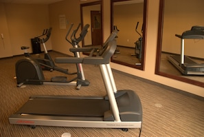 A fitness center with treadmills, elliptical machines, and a mirrored wall.