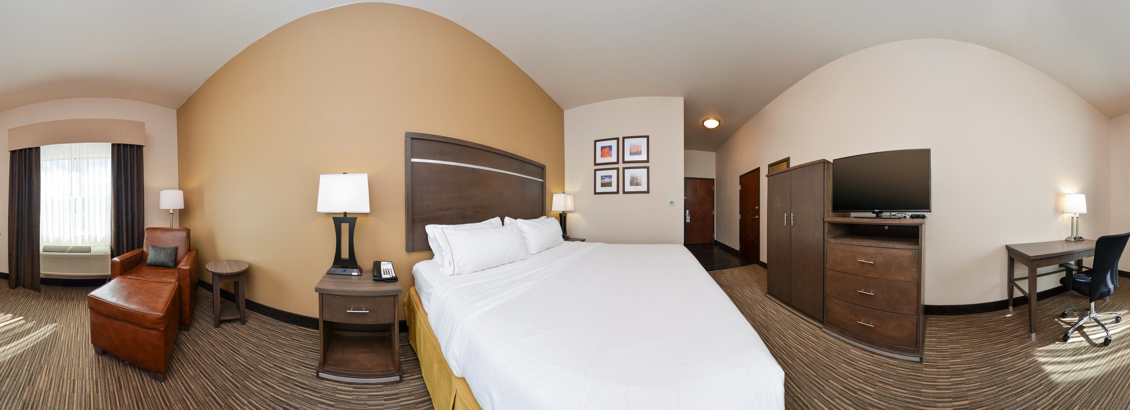 A hotel room with a large bed, a desk, a chair, a TV, and a wardrobe.