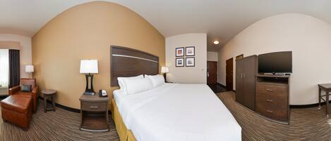 A hotel room with a large bed, a desk, a chair, a TV, and a wardrobe.