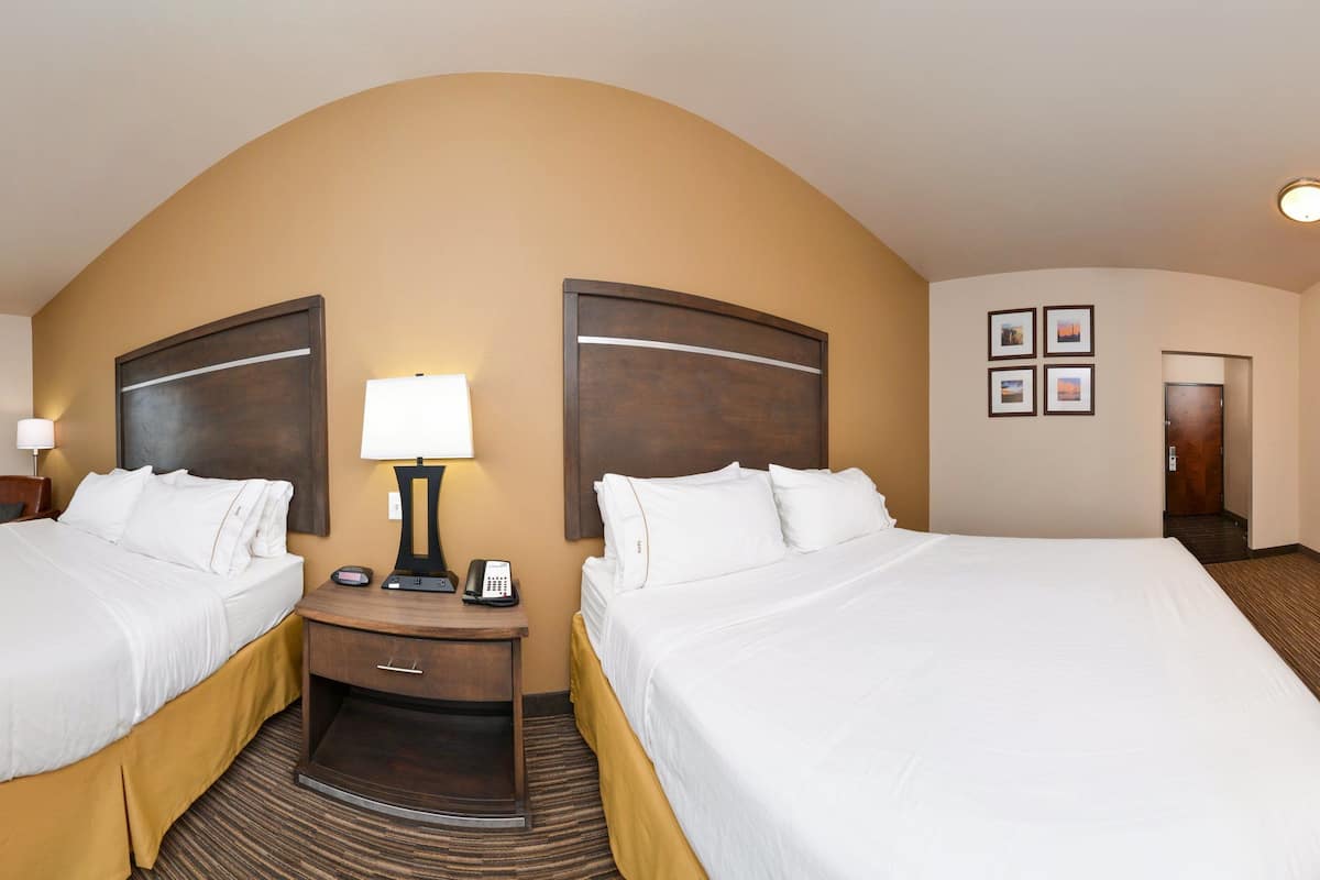 A hotel room with two beds, a desk, a chair, a TV, a lamp, and a wardrobe.
