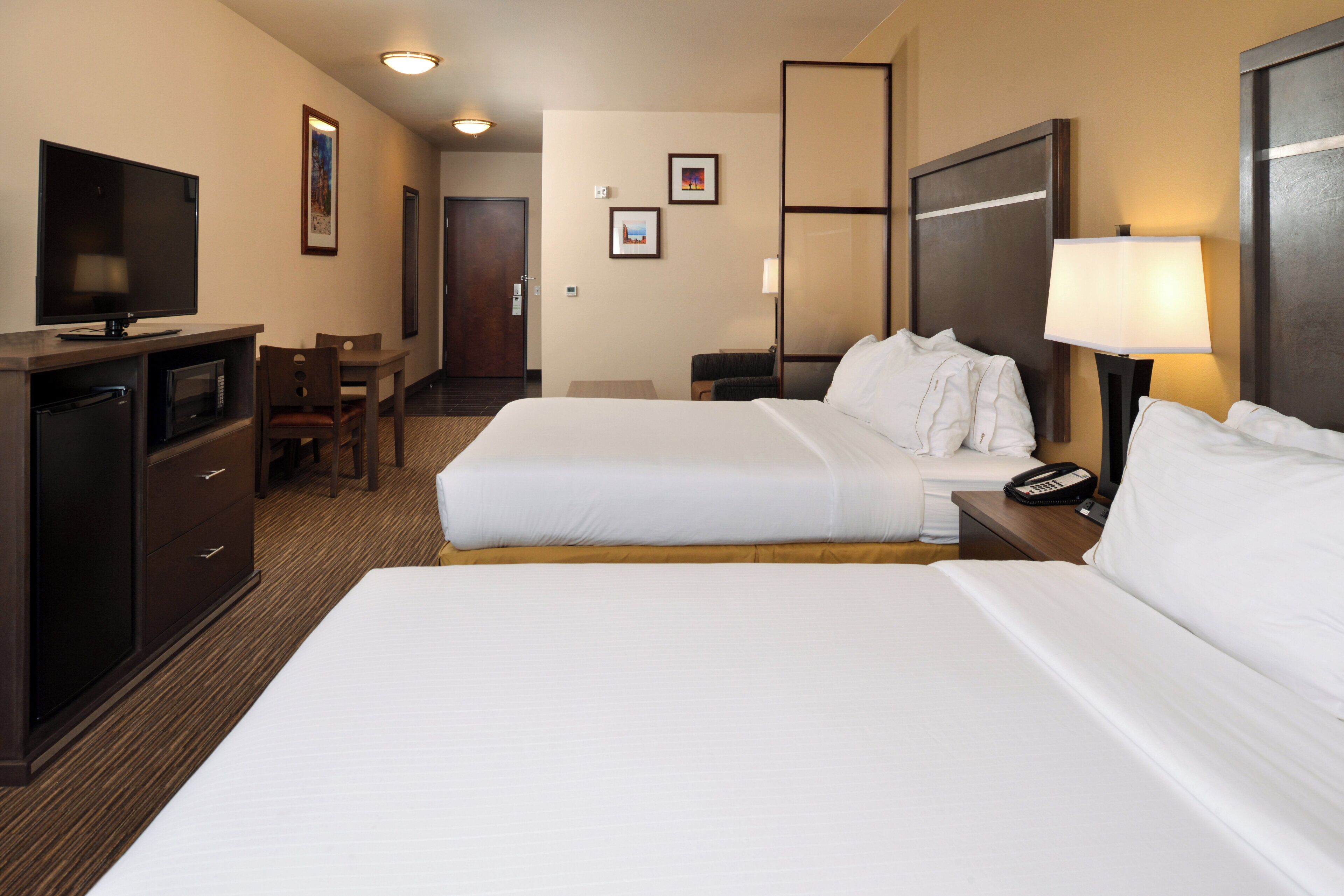 Une chambre d’hôtel avec deux lits, un bureau avec une télévision, une chaise, une table de chevet avec une lampe et un téléphone.