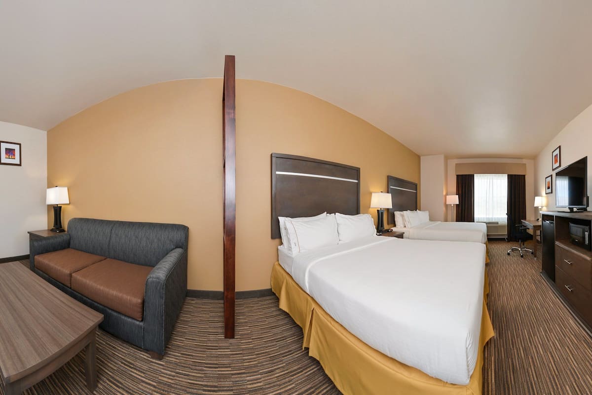 A hotel room with a large bed, a desk, a TV, and a sofa.