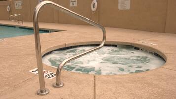 A hot tub with a metal ladder, surrounded by a tiled deck.