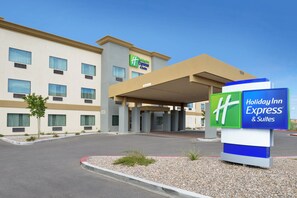 A Holiday Inn Express & Suites building with a clear sky, a covered entrance, and a signboard.