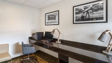 A reception desk with a computer, printer, and desk lamp. There are framed pictures on the wall and a patterned carpet.