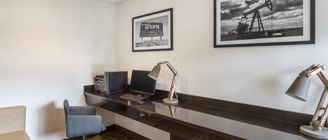 A reception desk with a computer, printer, and desk lamp. There are framed pictures on the wall and a patterned carpet.