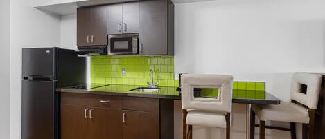 Una cocina compacta con armarios de madera oscura, un refrigerador negro, un microondas y un salpicadero de azulejos verdes. Cuenta con un pequeño mostrador con dos sillas.