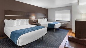 Une chambre d’hôtel avec deux lits, un bureau, une chaise, une grande fenêtre avec stores et un téléviseur à écran plat.