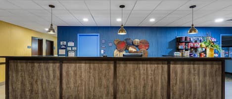 A reception desk with a wooden finish, a blue wall with decorative plates, and a shelf with various items.