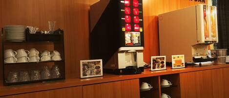 A drink bar with a coffee machine, tea station, and various cups and saucers on shelves.