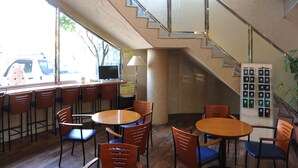 A restaurant with wooden tables and chairs, a staircase, and a view of the street outside. - Suizenji Comfort Hotel (Kumamoto)