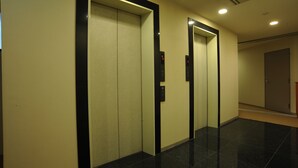 A hallway with three elevator doors, each with a control panel and a digital display. - Suizenji Comfort Hotel (Kumamoto)