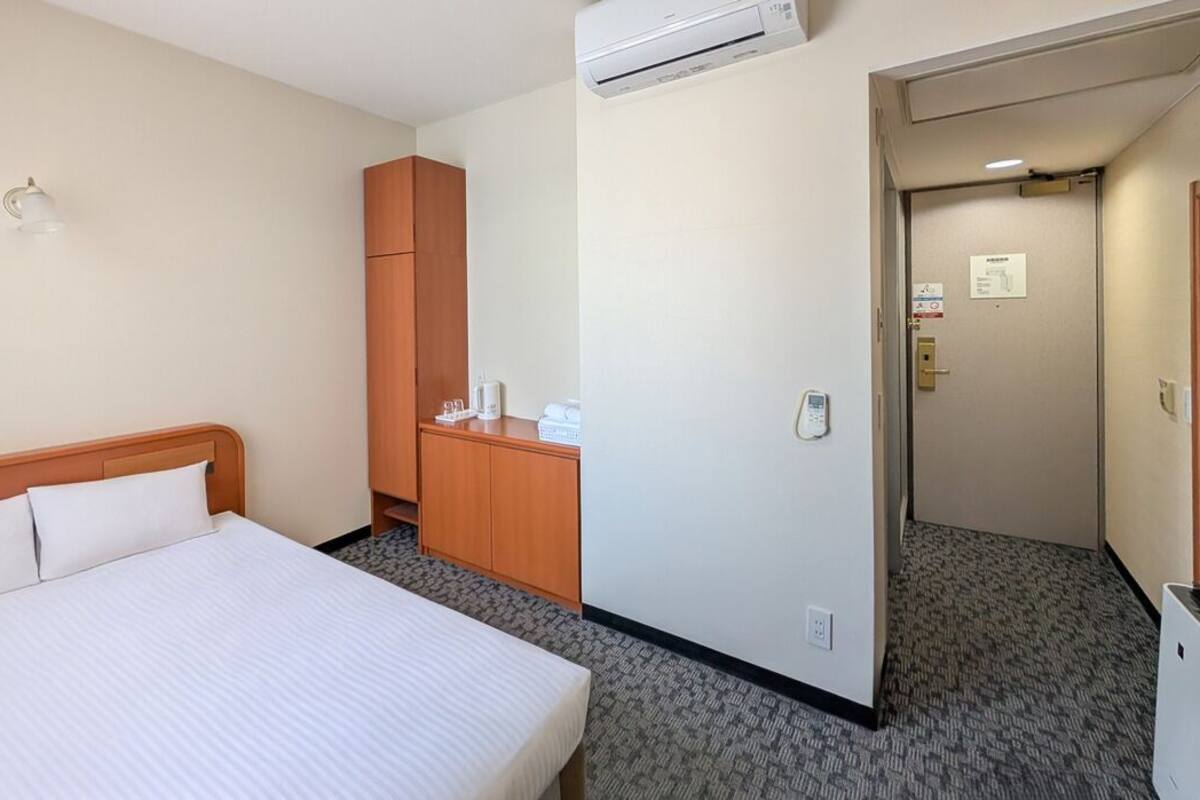Ein Hotelzimmer mit einem Bett, einem Schrank, einem Schreibtisch mit Stuhl und einer Klimaanlage.