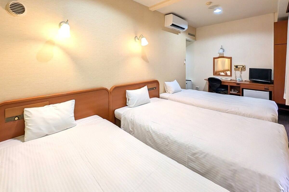 Ein Hotelzimmer mit zwei Betten, einem Schreibtisch mit Stuhl, einem Fernseher und einer Klimaanlage.