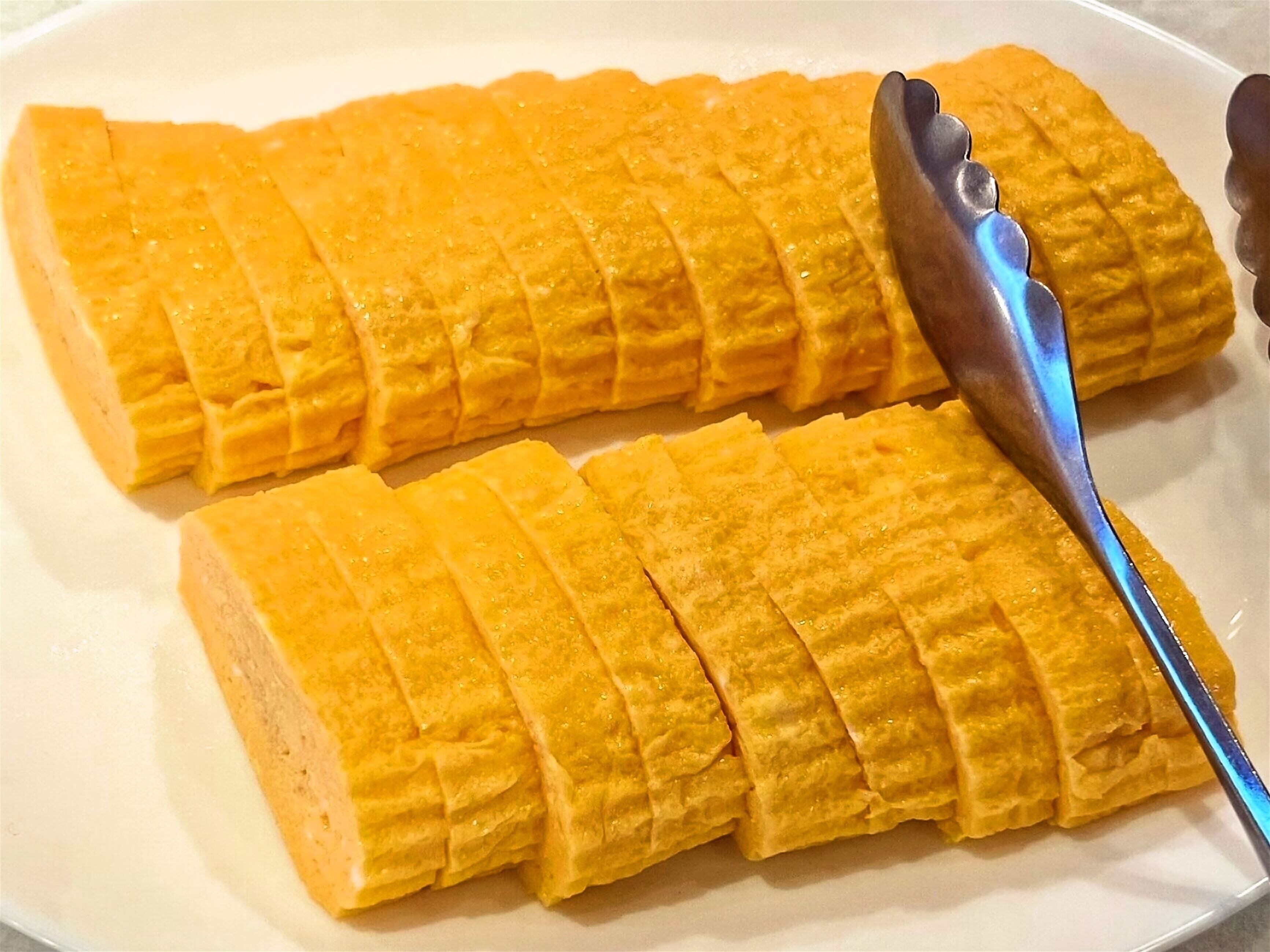 A rectangular plate with a yellow food item, possibly a cake or pastry, cut into strips.