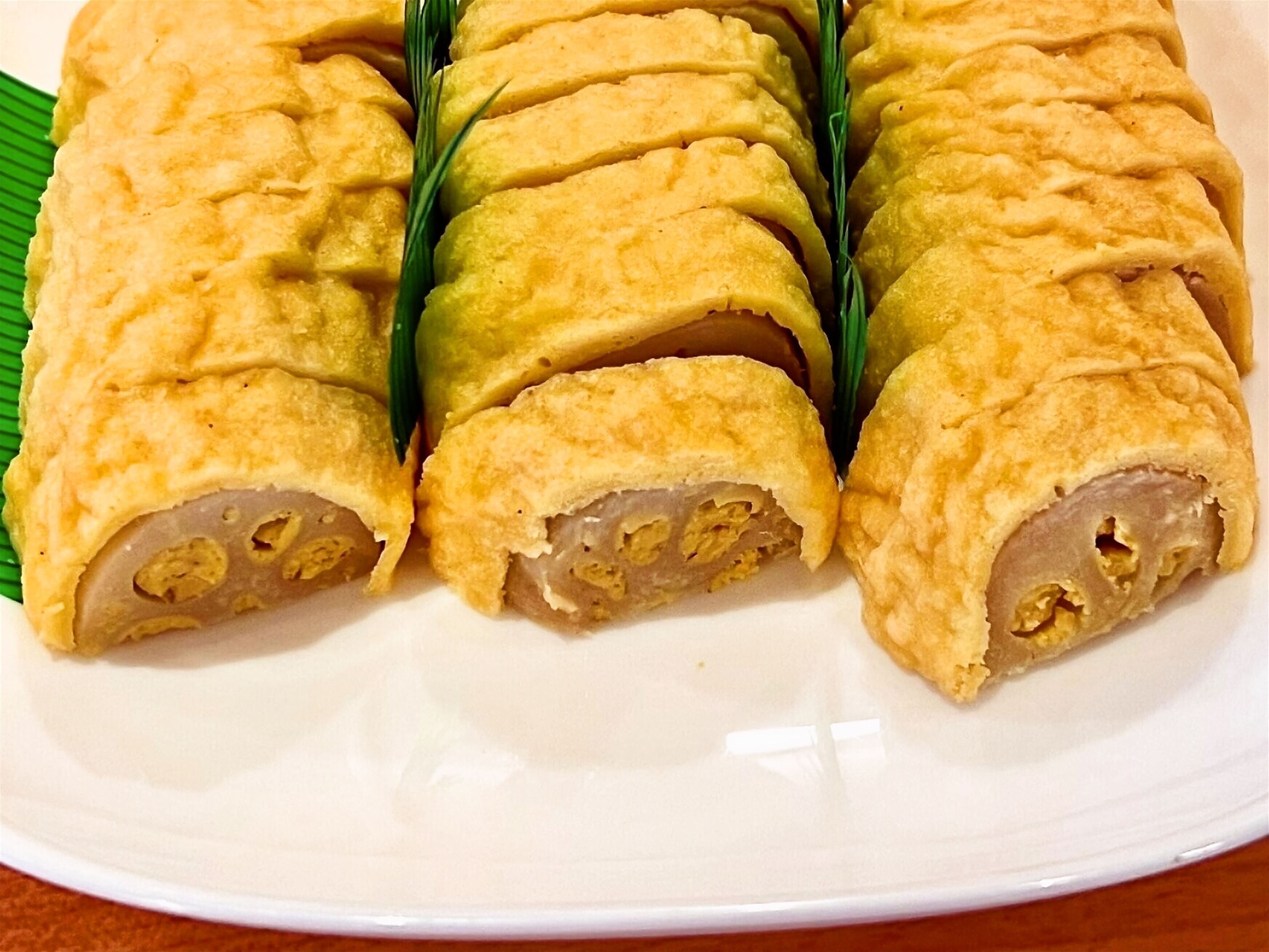 A plate of rolled pastries with a golden-brown crust, arranged on a white plate with a green leaf underneath.