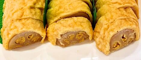 A plate of rolled pastries with a golden-brown crust, arranged on a white plate with a green leaf underneath.