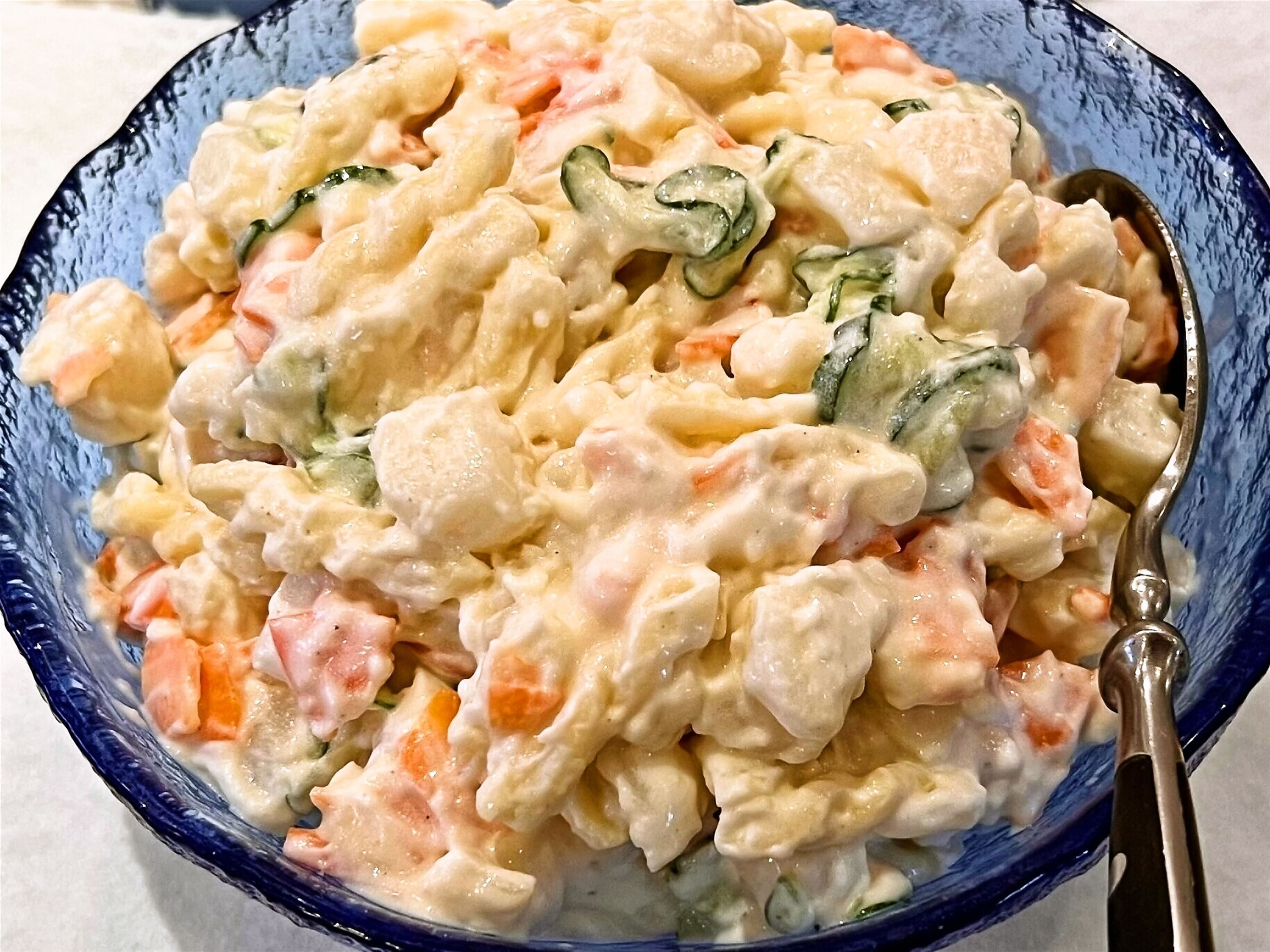 A bowl of potato salad with visible chunks of vegetables and a creamy dressing.