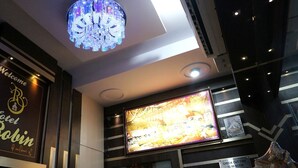 A hotel lobby with a large chandelier, a welcome sign, and a television screen displaying a room. - Hotel Robin (Amritsar)