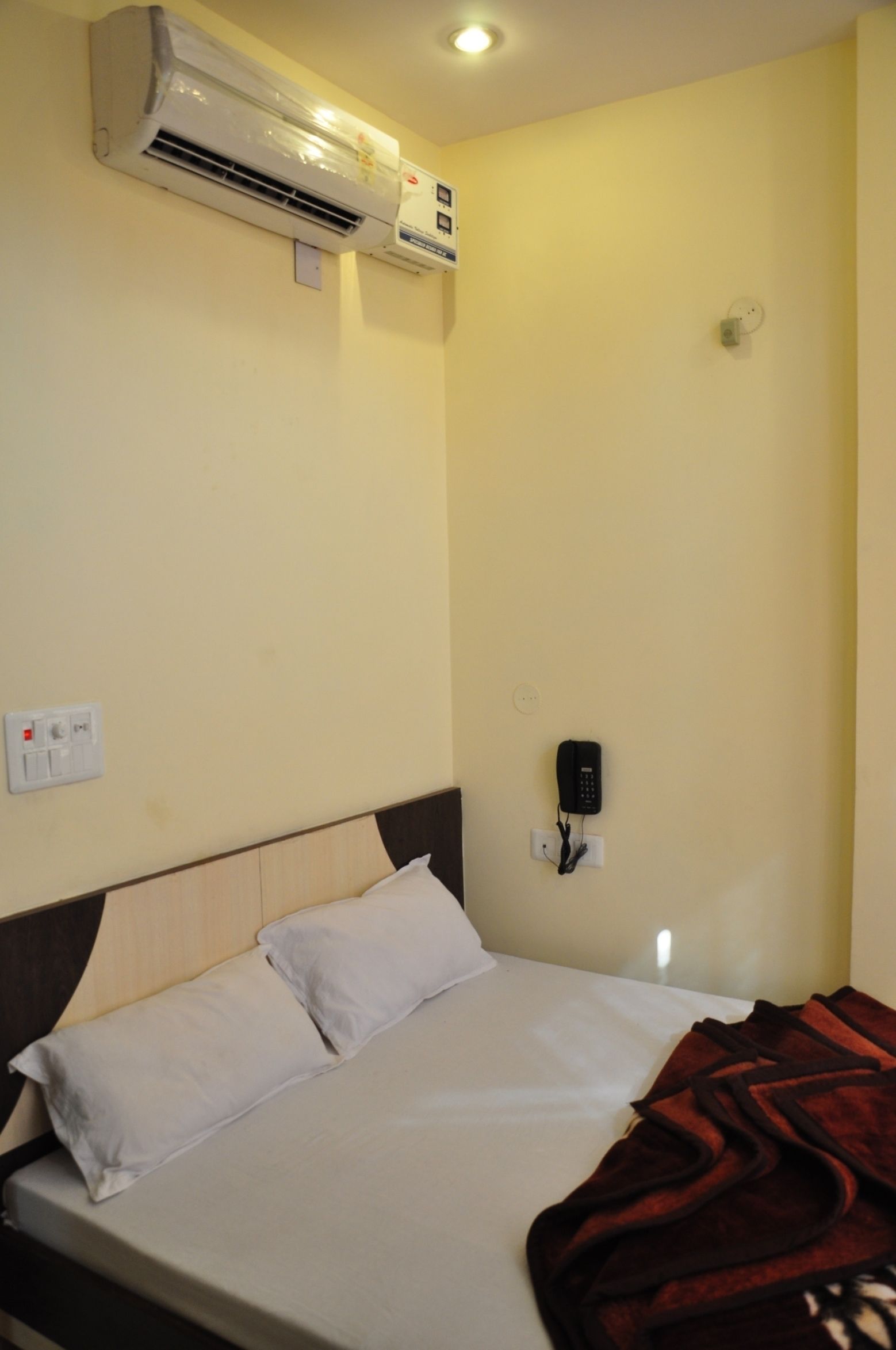 Habitación de hotel con una cama, un equipo de aire acondicionado, un teléfono y un enchufe en la pared.