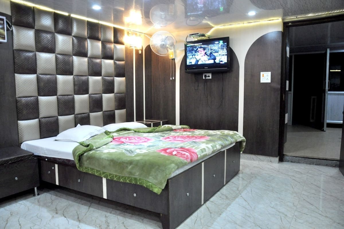 A bedroom with a bed, a TV mounted on the wall, and a fan.