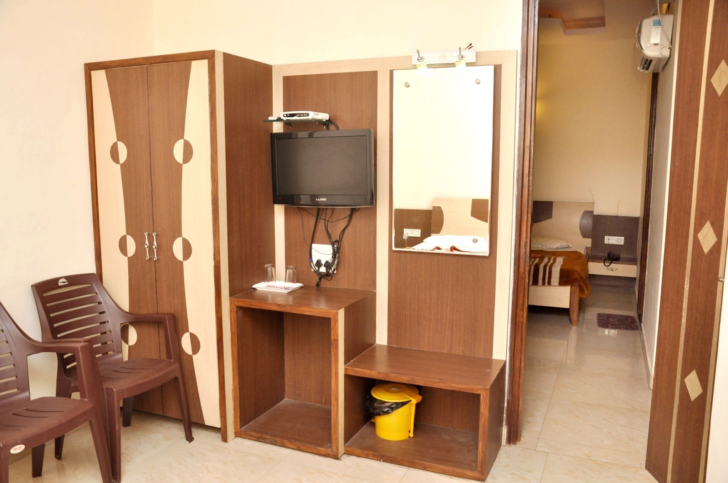A room with a wardrobe, a television, a desk, and a bed.