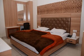 Une chambre avec un grand lit, un bureau, une chaise et une table de chevet sur laquelle se trouve une bouilloire.