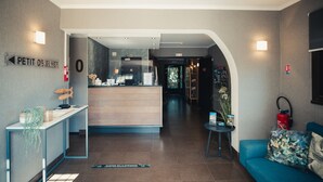 A hotel lobby with a reception desk, a blue sofa, and a small table with a plant. - Van der Valk Hotel Le Catalogne Saint Aygulf (Fréjus)