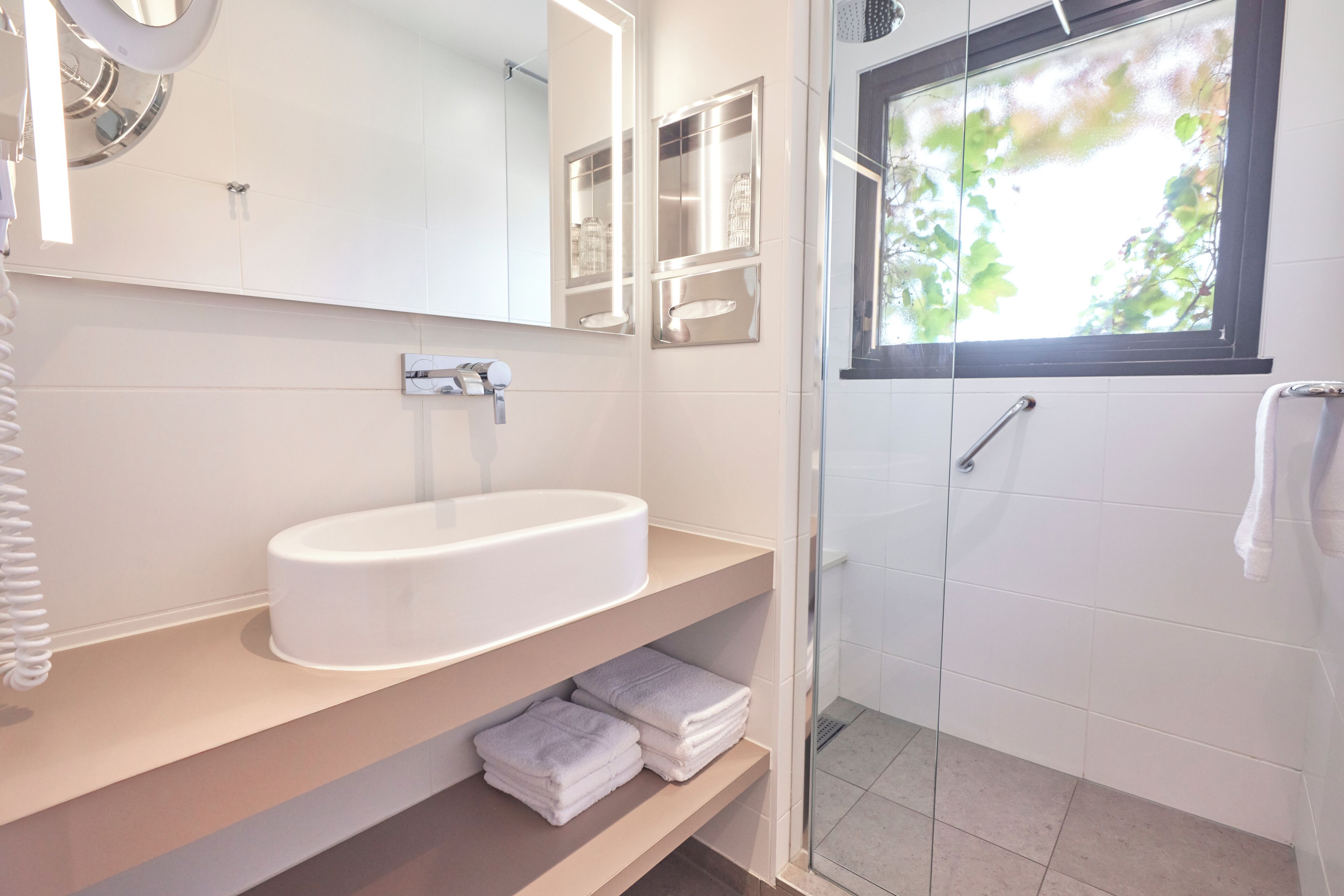 Une salle de bain moderne avec un lavabo blanc, un miroir et une douche en verre.