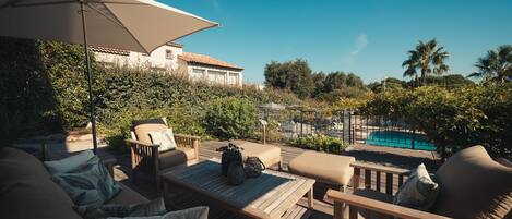 Eine Terrasse im Freien mit Pool, Holzmöbeln und Blick auf ein Haus im Hintergrund.