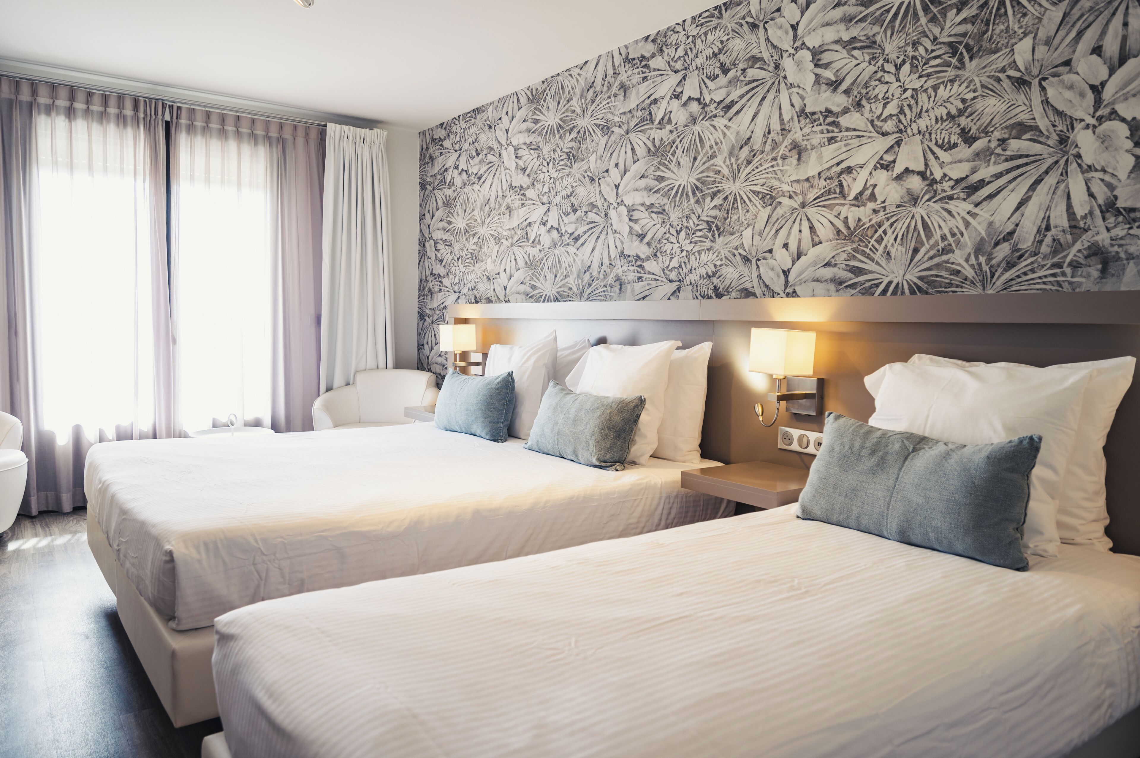 A hotel room with two beds, a large floral-patterned wall, and a window with curtains.