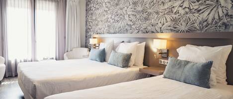 Ein Hotelzimmer mit zwei Betten, einer Wand mit großem Blumenmuster und einem Fenster mit Vorhängen.