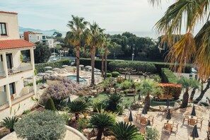 A courtyard with outdoor seating, palm trees, and a pool. - Van der Valk Hotel Le Catalogne Saint Aygulf (Fréjus)