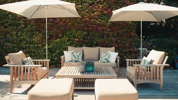 An outdoor seating area with two wooden chairs, a sofa, and a table, all under white umbrellas.