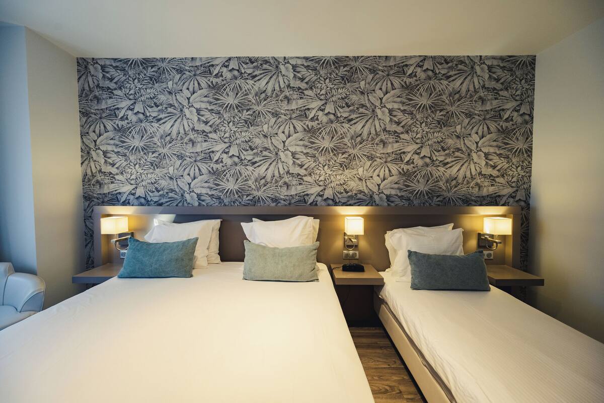 Hotellihuone, jossa on kaksi sänkyä, kuviollinen seinä, yöpöytälamput ja yöpöytä.