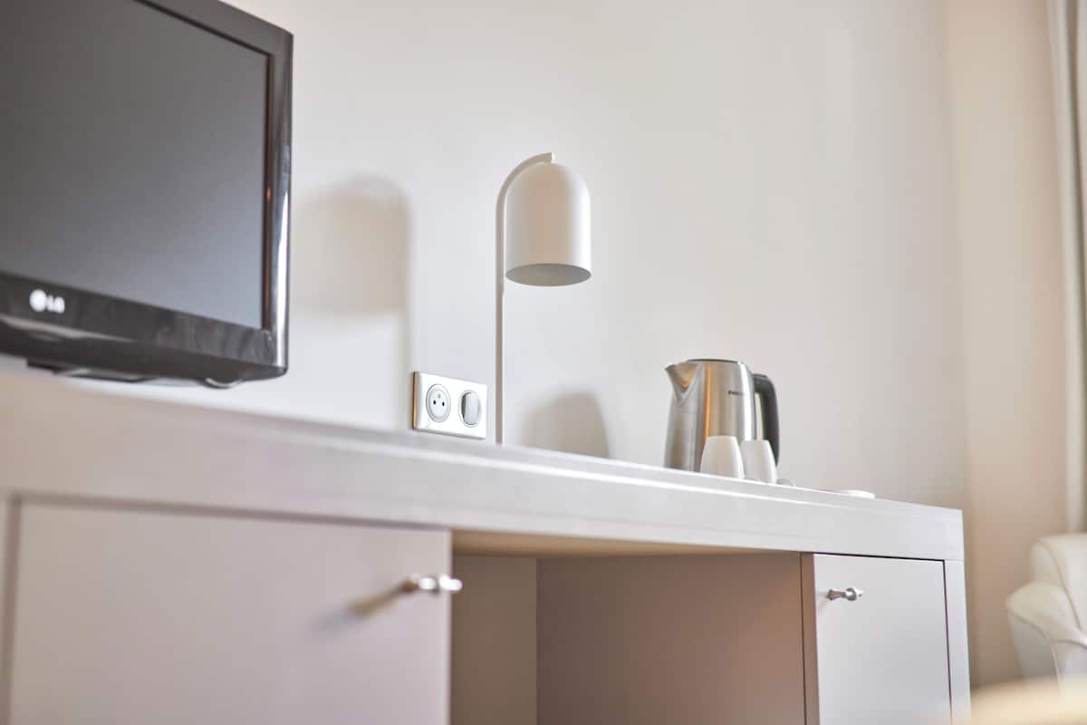 Moderni hotellihuone, jossa on taulutelevisio, valkoinen lamppu, kahvinkeitin ja lipasto, jossa on yksi laatikko.