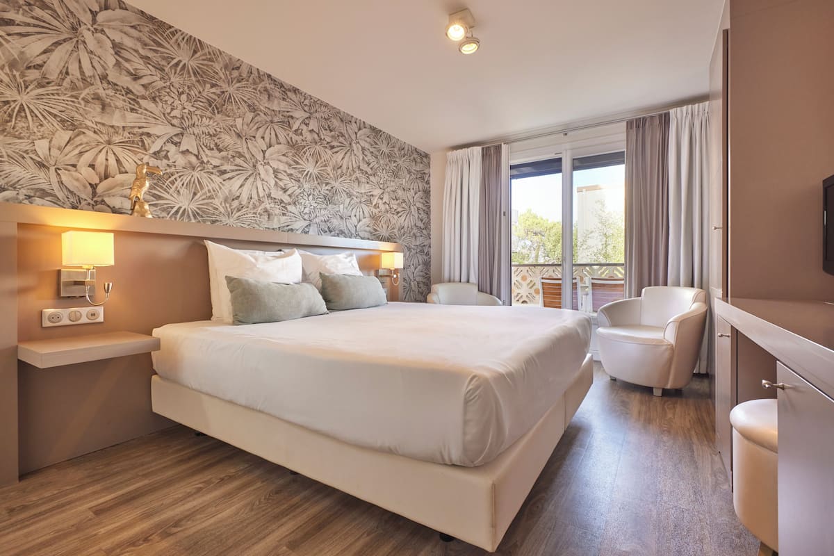 Moderni hotellihuone, jossa on suuri sänky, oleskelualue tuolilla, televisio ja parveke, jossa on verhot.