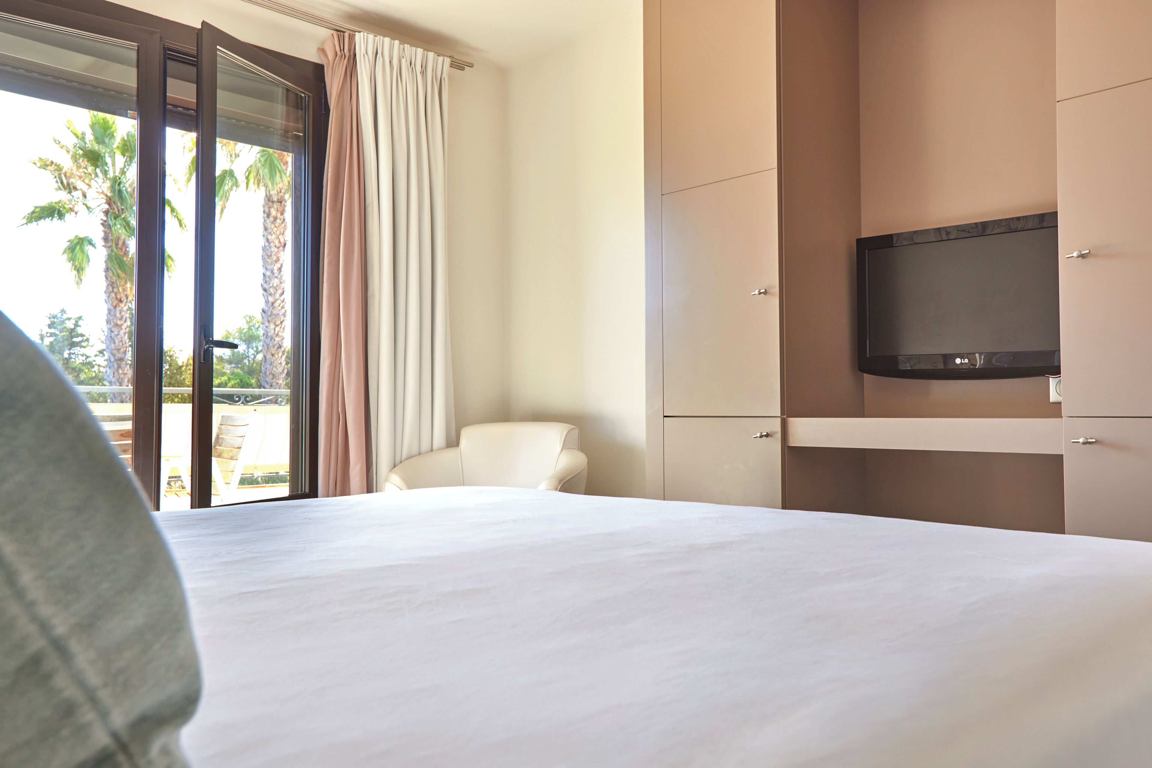 Habitación de hotel con cama, televisor, una silla y un ventanal corredero con cortinas.