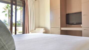 Habitación de hotel con cama, televisor, una silla y un ventanal corredero con cortinas.