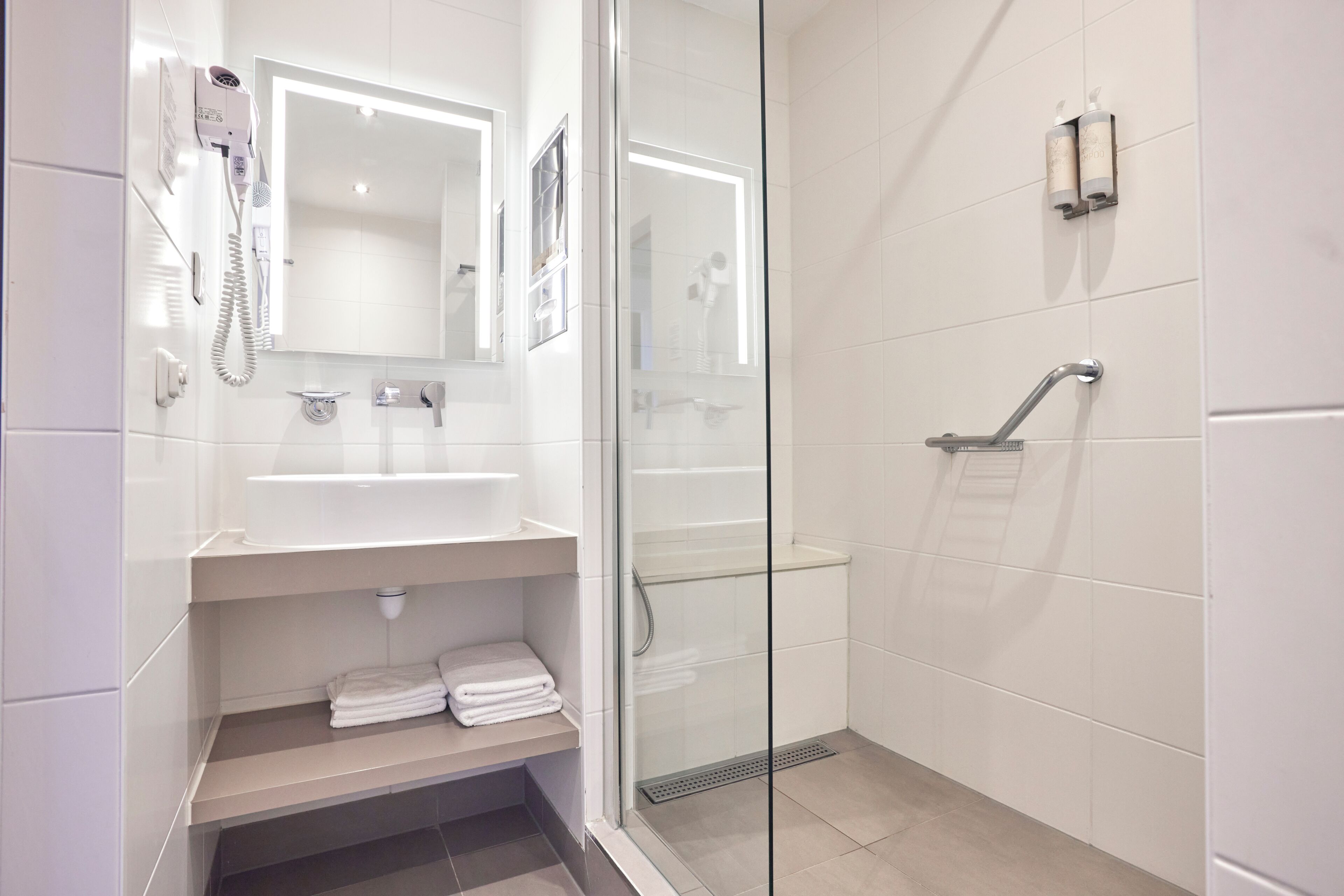 A modern bathroom with a glass shower enclosure, a hairdryer, and a towel rack.