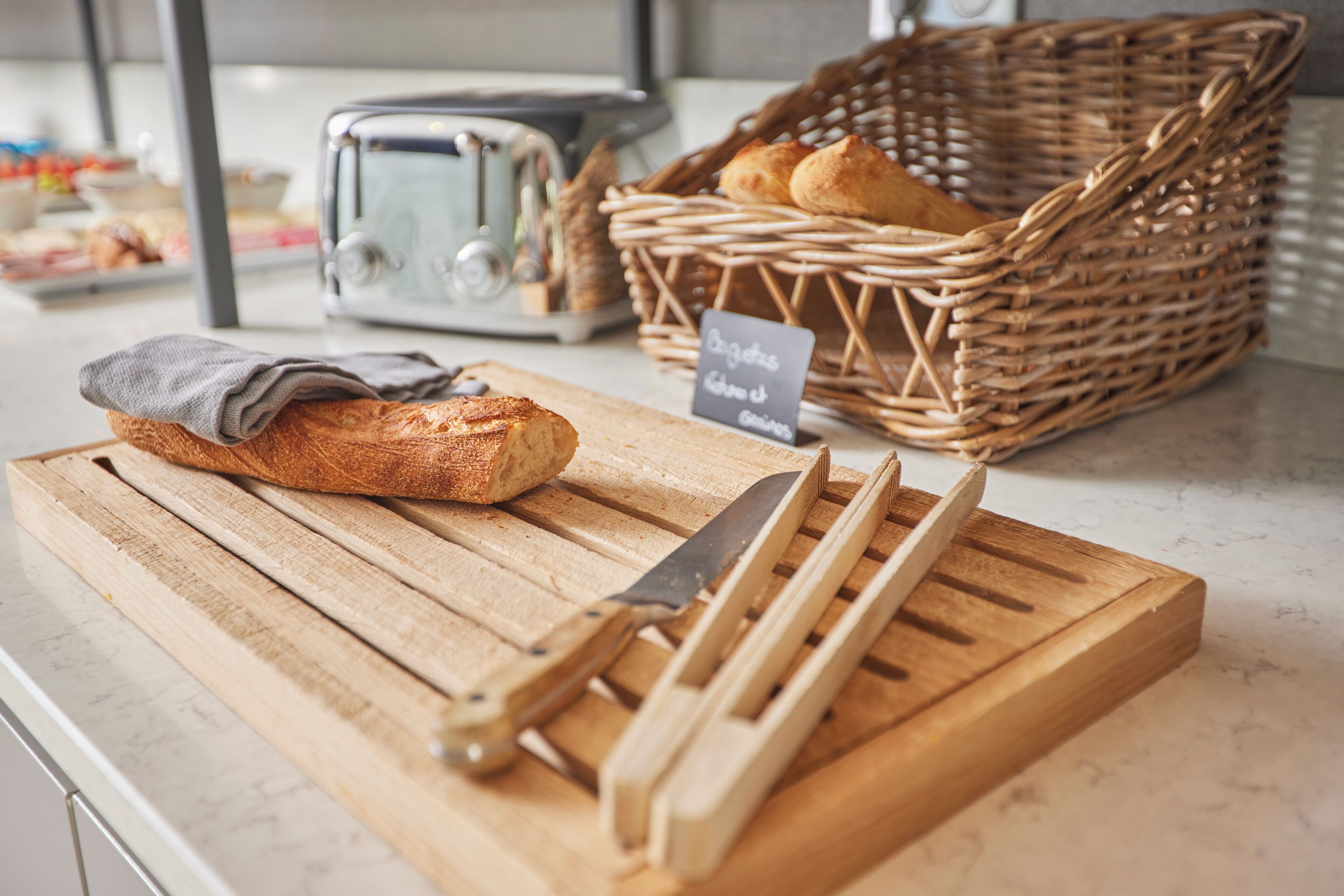 A kitchen counter with a loaf of bread, a knife, and a basket of bread.