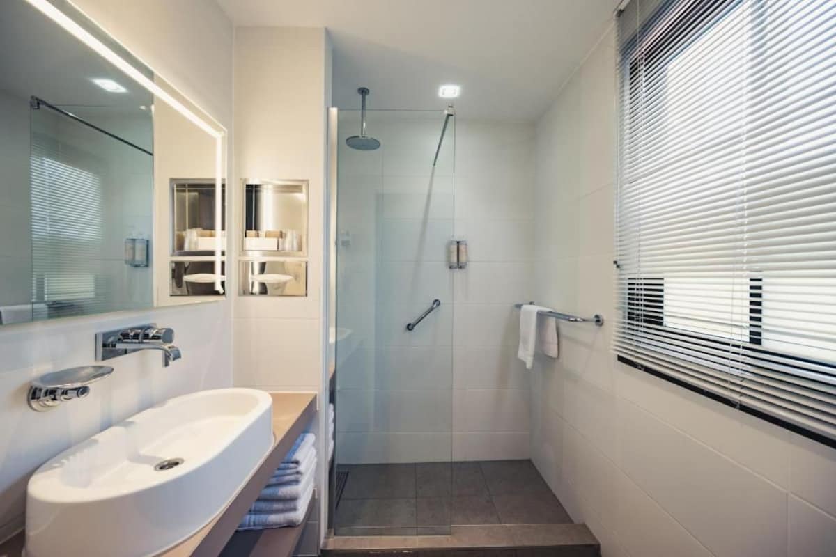 A modern bathroom with a glass-enclosed shower, a white sink, and a large mirror.