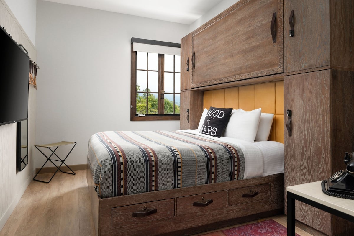 A bedroom with a bed, wooden wardrobe, and a small table with a telephone.
