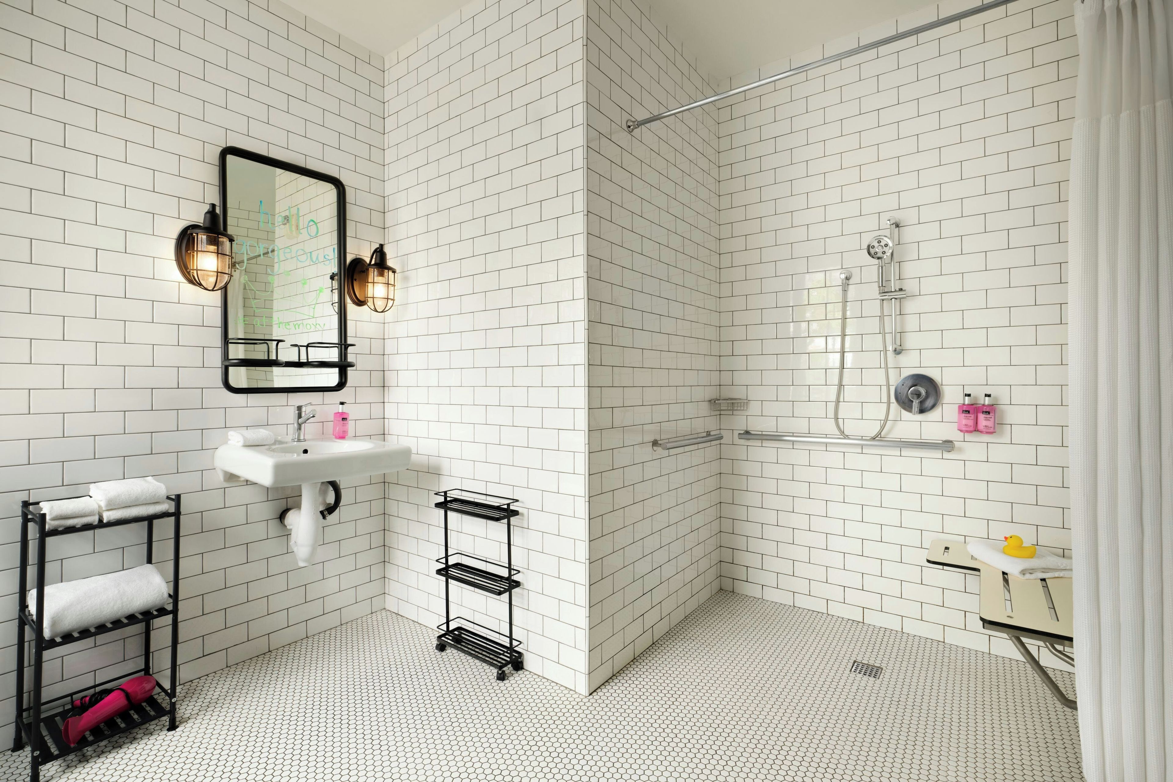 A modern bathroom with white subway tiles, a white sink, a mirror, and a shower area.