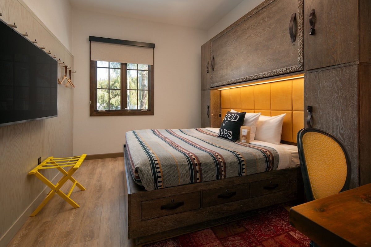 A bedroom with a bed, wooden headboard, a window, and a wooden cabinet.