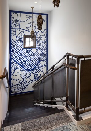 Una escalera con un muro estampado en azul y blanco, una pequeña ventana y una lámpara colgante.